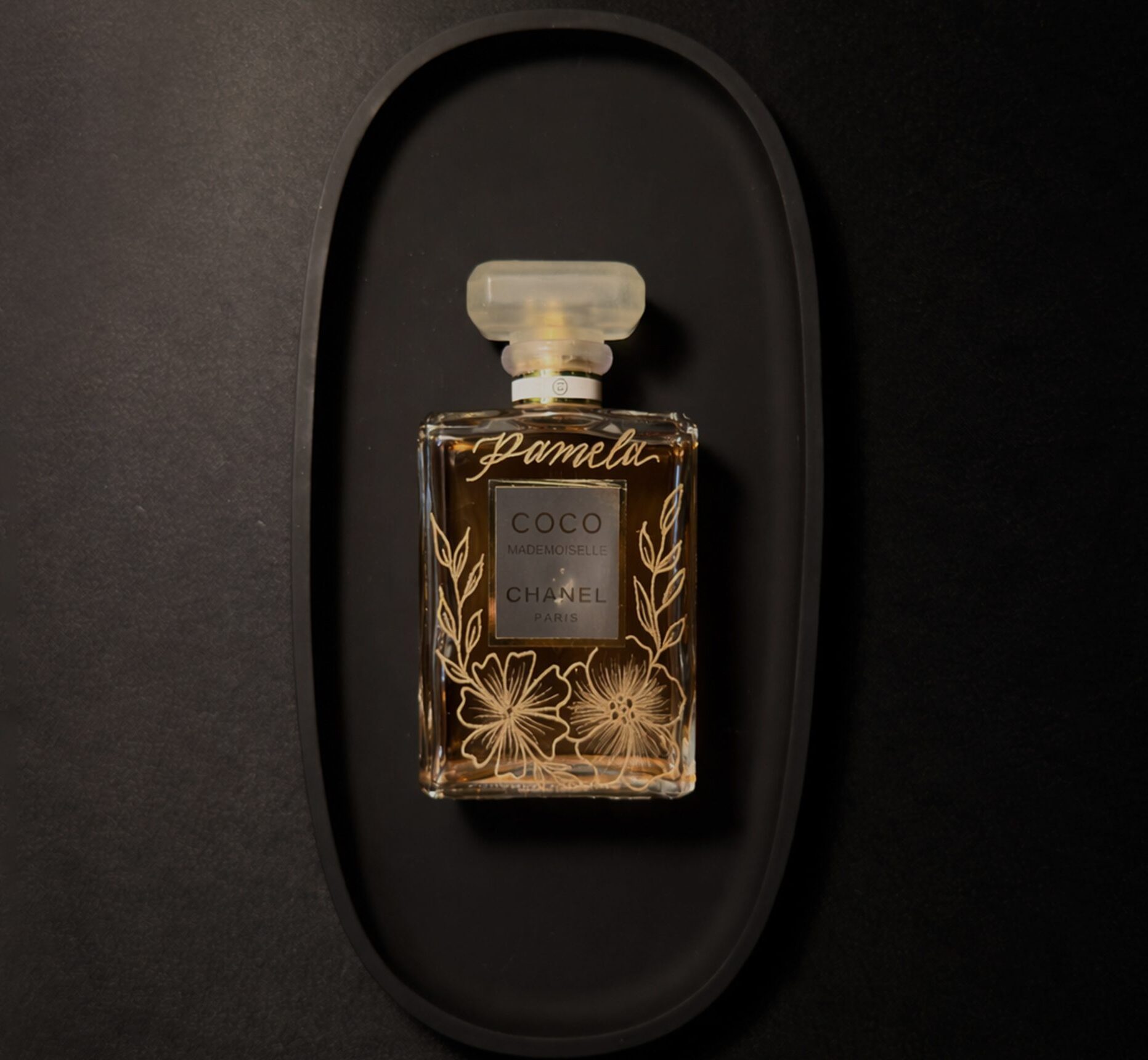 Elegant perfume bottle with dried flowers inside on a black tray.