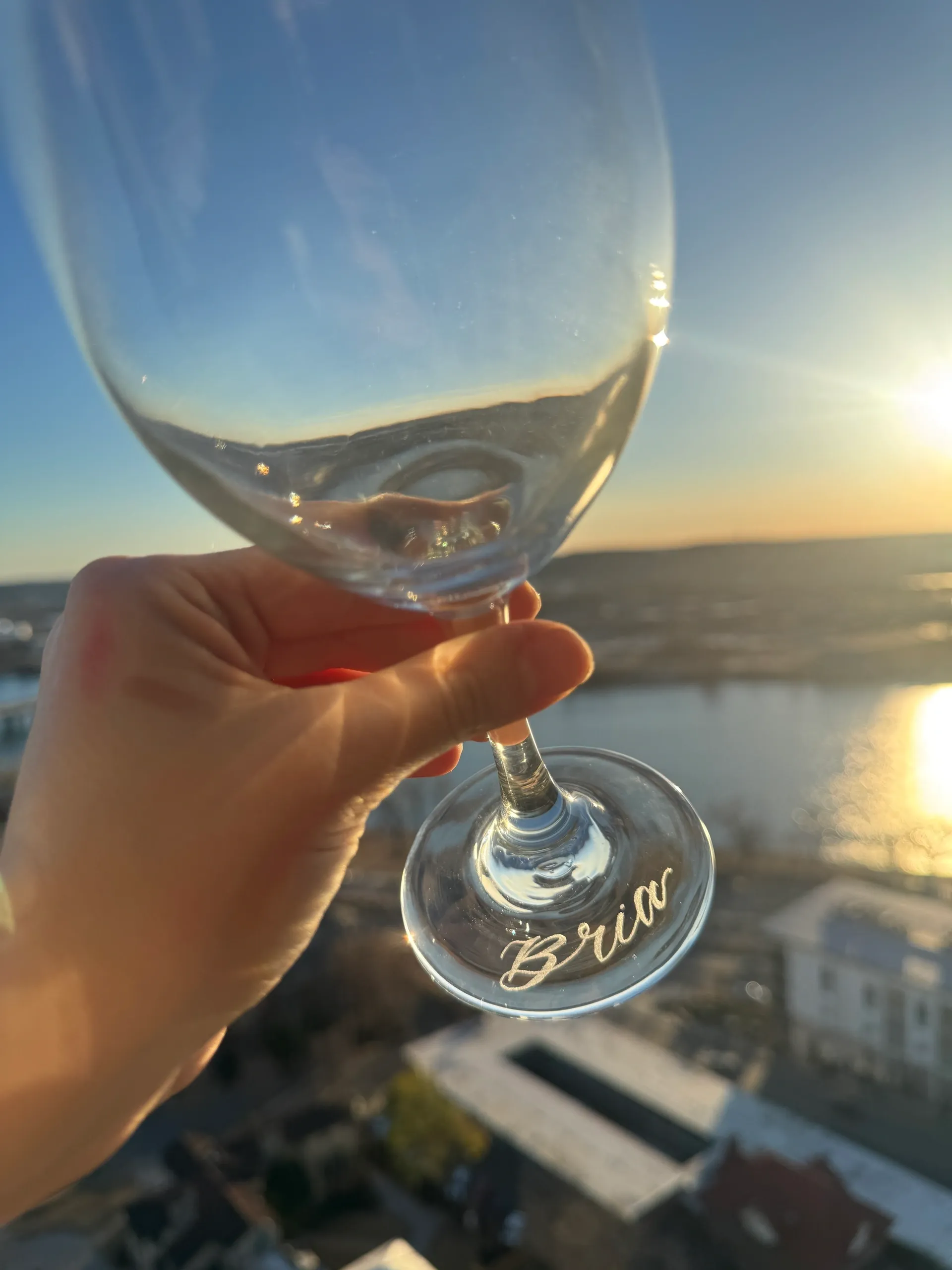 Hand holding a wine glass with a sunset and cityscape background.