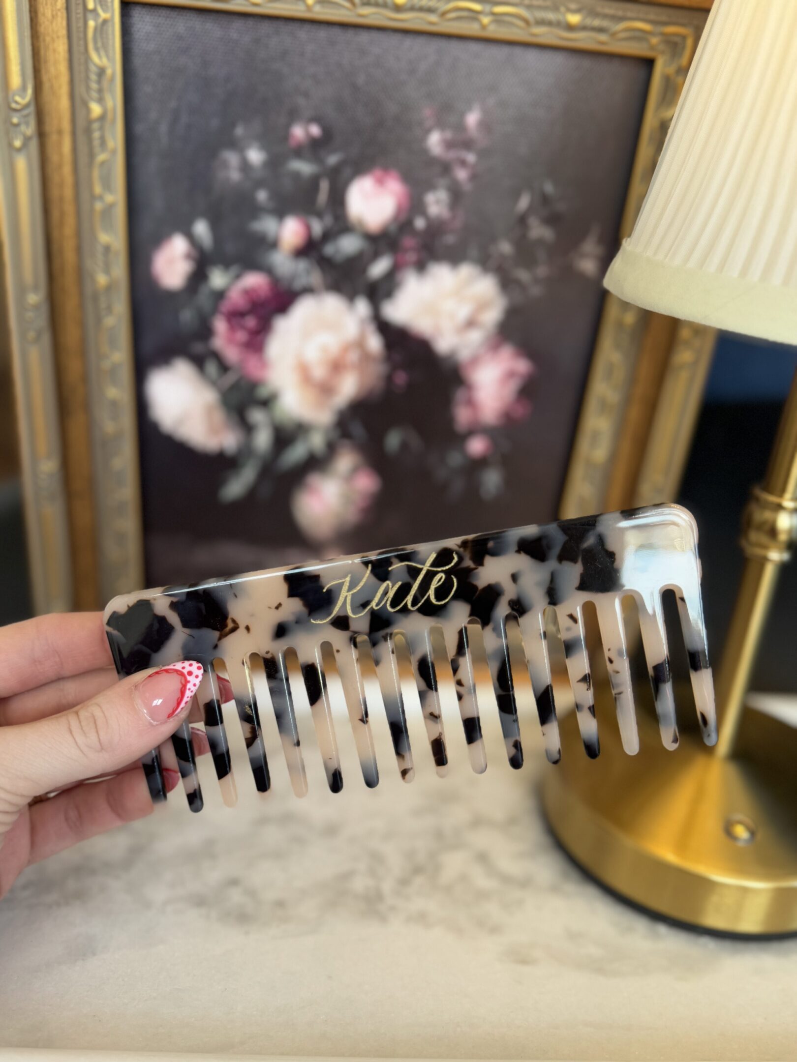 Hand holding a tortoiseshell comb with floral background.
