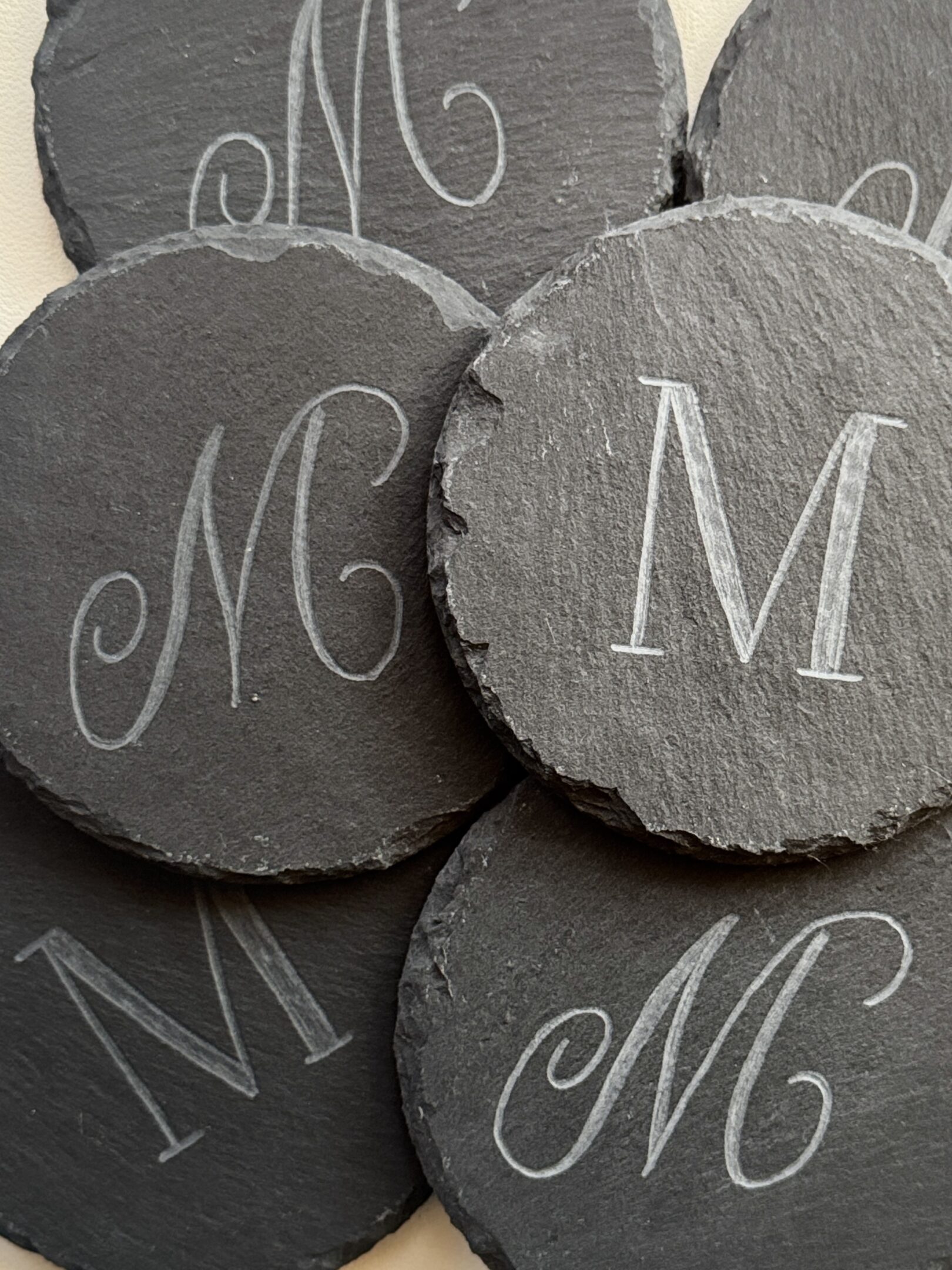 Round slate coasters with the letter 'M' in elegant script.