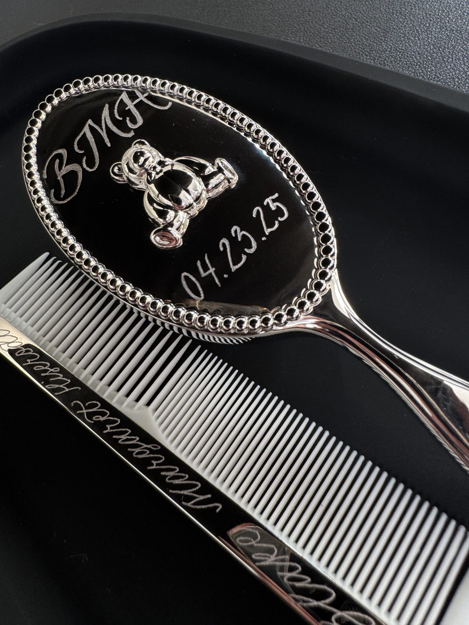 Engraved silver hairbrush and comb set with personalized initials and date.