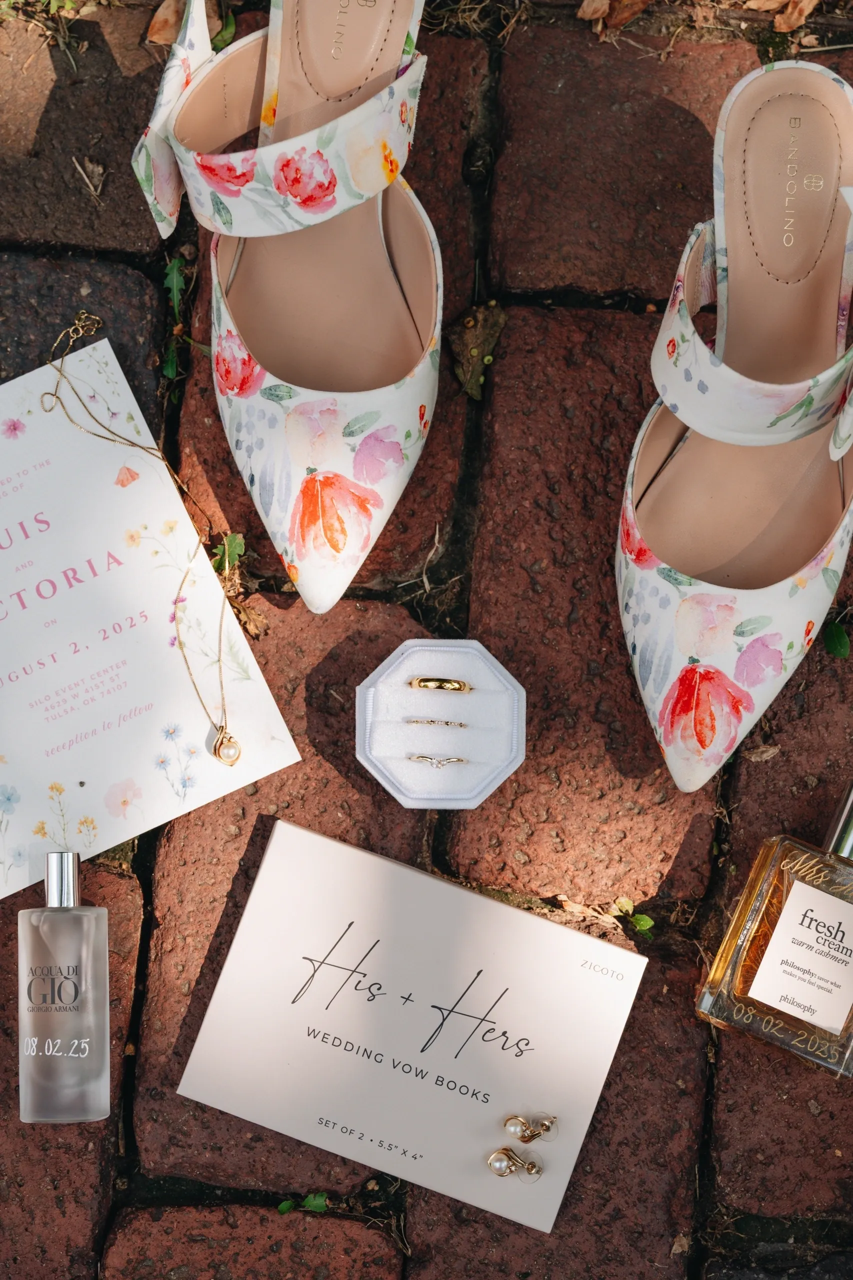Floral shoes with wedding ring box and invitation on brick ground.