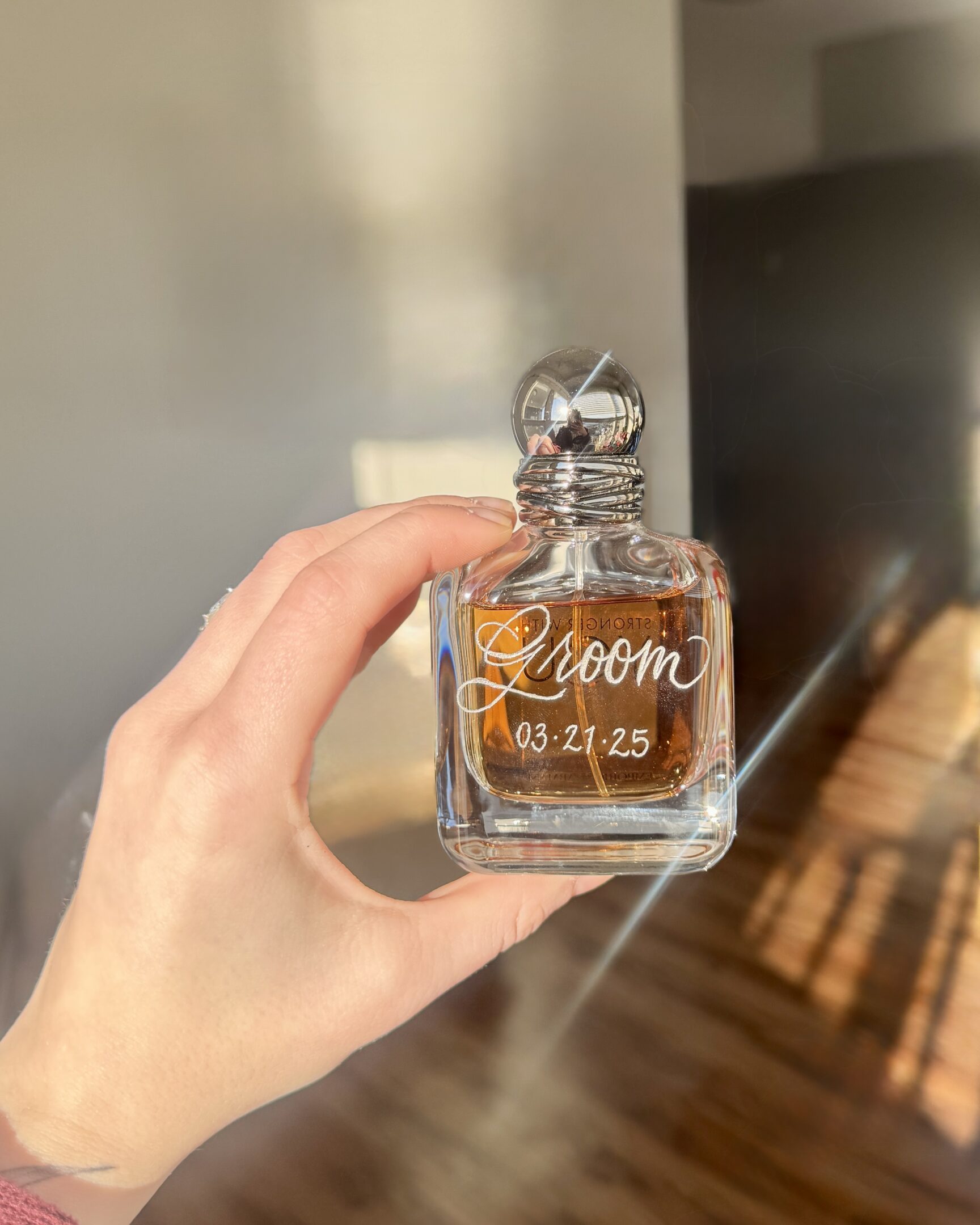 Hand holding a perfume bottle labeled "Zoom 2.0" in sunlight.